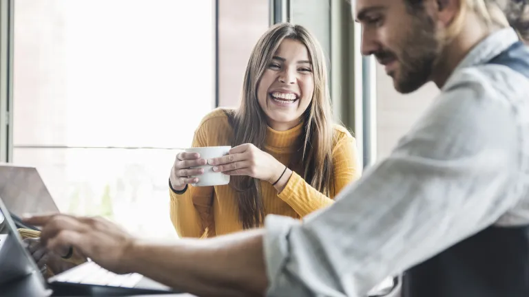 Image montrant une collègue avec son café au bureau de son collègue qui est devant son pc